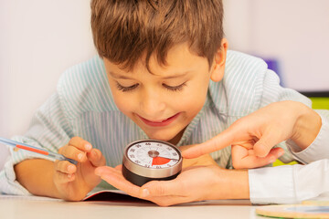 Boy with autism spectrum disorder during ABA therapy look at lesson timer in teachers hands...
