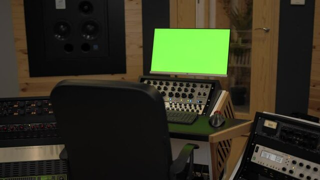 empty sound design mastering studio with all mixers on and monitor with green chromakey
