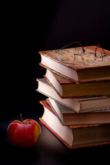 Fünf alte Bücher mit einer Brille und einem Apfel bei stimmungsvollem Licht