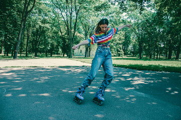 Beautiful teenager girl performs tricks on roller skates in the park on a summer day