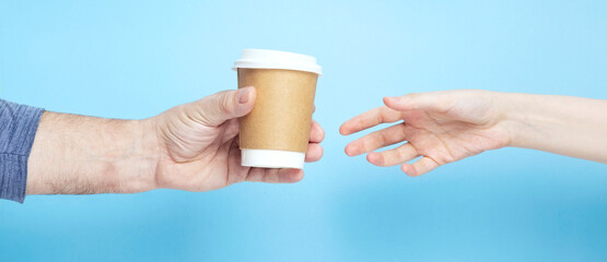 Male holds hand paper cup with coffee female takes cup on blue background