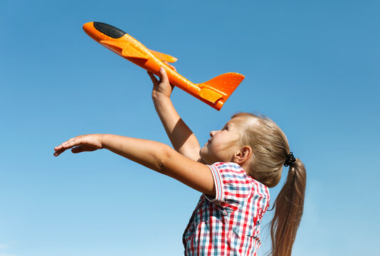 Child girl playing with orange toy airplane. Photo against a blue sky.
