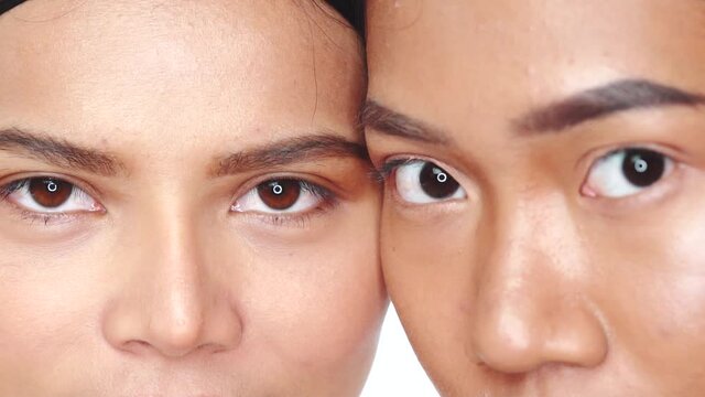 Closeup faces ot two beautiful Asian women opening eyes and looking at the camera over white background. Natural beauty. Skin care cosmetics