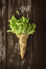 Lettuce leaveson in a paper bag a wooden dark table. Batavia salad. Authentic still life with green salad flat lay. Rustic style Top view