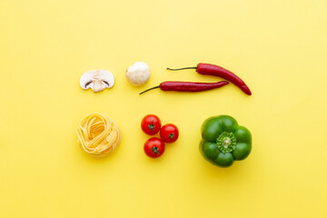 Tagliatelle raw pasta and vegetables  on yellow background, top view. Copy space, cooking recipe