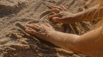 Woman's hand draws on the sand on a sunny day during sunset