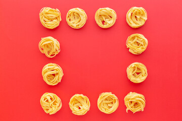 Tagliatelle raw pasta nests on red background, top view.