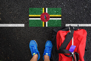 a man with a shoes and travel bag is standing on asphalt next to flag of Dominica  and border 