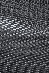 Texture of cambered metal perforated netted sheet with lighting effect.Grunge netted metal grill texture. Curved dark  metal rhombed mesh for abstract background.