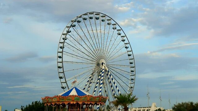 Man&egrave;ge pour enfants et grande roue sur fond de ciel bleu ennuag&eacute;.