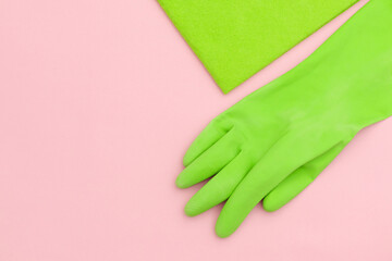 Green microfiber cloth and kitchen latex gloves on a light pink background, top view.