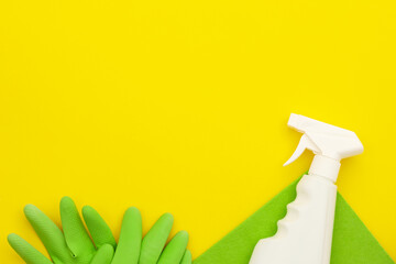 A cleaning spray lies on a green microfiber, green latex gloves near on a yellow background, top view, copy space. Cleaning supplies.