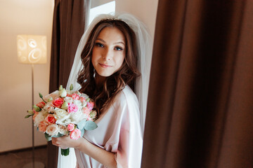 Morning of the bride in a pink robe and a veil in the hotel on the bed, wedding dress