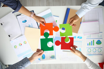 Businessmen hold multicolored puzzles in hand above table with commercial indicators. Small and...