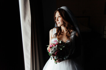 Morning of the bride in a pink robe and a veil in the hotel on the bed, wedding dress
