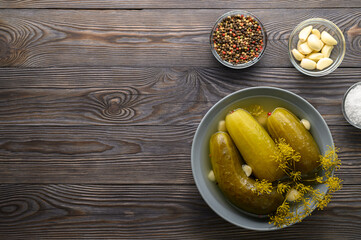 Healthy fermented food. Fermented cucumbers in a plate, garlic, dill and peppers in bowls on a dark wooden background. Space for text, top view.
