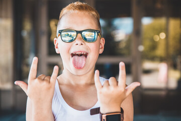 young boy in sunglasses sticks out his tongue.