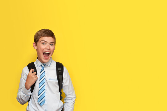 A boy in a shirt and tie with a school backpack emotionally rejoices, smiling on a yellow background.