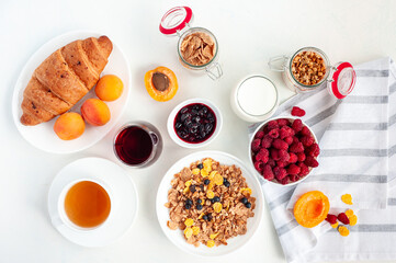 Light summer breakfast with muesli, milk, juice, apricots and raspberries on a light background. Flatly.