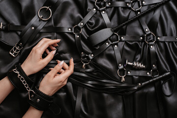 women's hands in handcuffs on a dark silk sheet next to adult toys