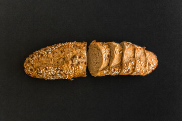 Wholegrain sliced freshly baked bread with flax and sesame seeds on black background. Top view