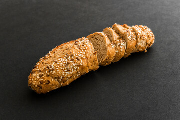 Wholegrain sliced freshly baked bread with flax and sesame seeds on black background. Top view