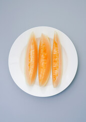 A plate of Xinjiang Hami melon on a white plate. Sweet and delicious Hami melon on a gray background
