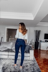 Beautiful model posing for photos in in clear room. Wearing jeans and a white blouse. 