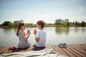 Happy Brother and sister sitting on the dock and eating a watermelon