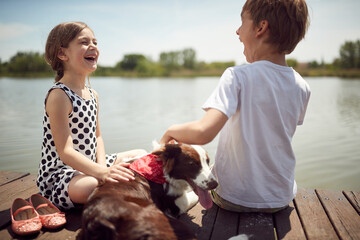 Cheerful brother and sister with their dog on the dock