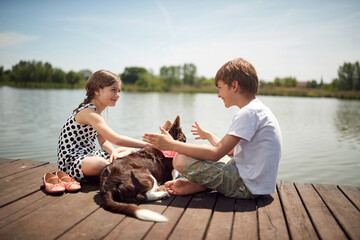 Brother and sister enjoying on the dock of the lake with their dog