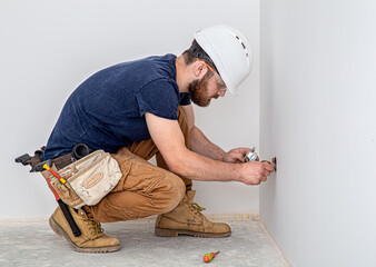 Electrician Builder at work, installation of sockets and switches. Professional in overalls with an...