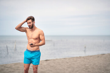 Fototapeta na wymiar Muscular man on the beach..Handsome man having fun on the beach by the sea and listen music.