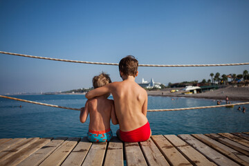 Two brothers sit on the pier and look at the sea