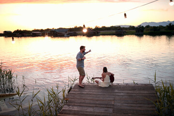 Romantic  couple plays guitar, singing and have fun on the river at sunset.