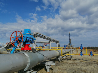 Pipeline fittings and manifold of producing gas wells in the field. Handwheels for high pressure valves. In the background, a drilling rig. Blurring distant objects.