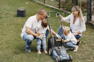 Mowing the grass with a lawn mower. Family cuts the lawn in the garden. Family with sons.