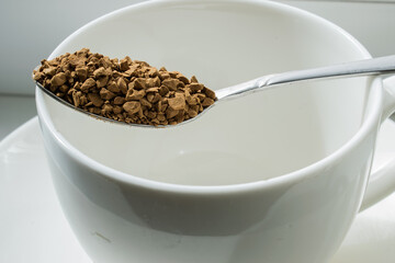 a metal spoon full of dry crumbly coffee lies on a white Cup that stands on a saucer