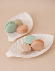 Macarons in white plate on beige background.

