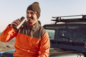 Young man traveler drinking from his thermocup while halt on a hike