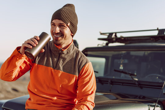 Young man traveler drinking from his thermocup while halt on a hike