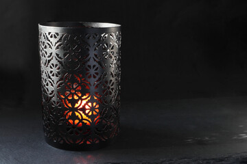 a luxury black stencil metal candle holder with a lighting scented candle are displayed on the blak...