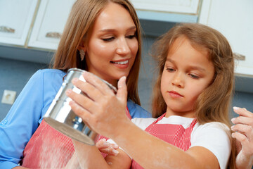Mother and her little daughter preparing dough in kitchen
