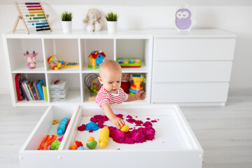 Baby playing with kinetic sand and sand toys. Little girl playing with sand at home, games,...