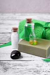 Obraz na płótnie Canvas Spa set: massage stone, essential oil, sea salt, green gel, organic soap and green towel on white wooden table 