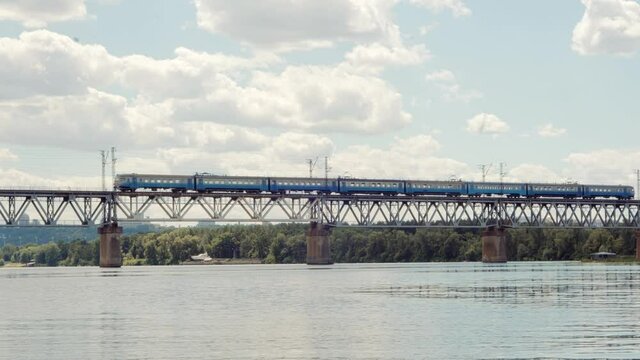 Cargo Train Moving On Railroad Bridge.Kiev City Bridge.Freight Train Passing Through Dnieper River.Electric Locomotive With Wagons Rides On Steel Railway.Heavy Industry Transportation Concept.