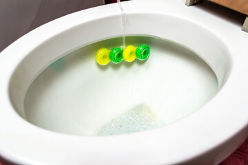 A woman's hand in a rubber glove cleans the toilet bowl with a brush, sink