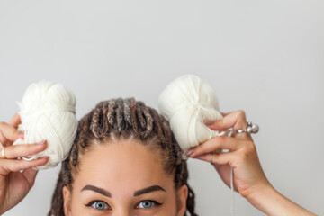 A beautiful young girl knitter smiles and holds skeins of white yarn in her hands, applying them to...