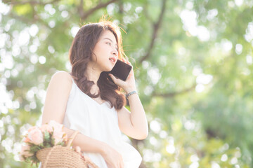 Fototapeta premium Cheerful young woman talking smartphone in city green park