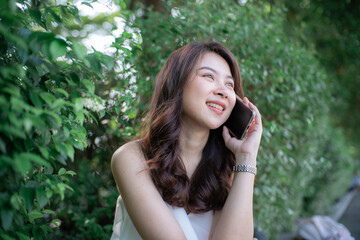 Cheerful young woman talking smartphone in city green park